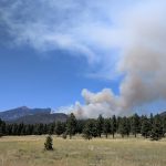 A smoke plume coming up on the east side of a peak.