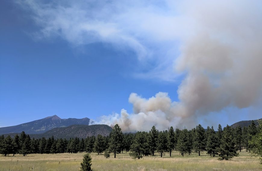 A smoke plume coming up on the east side of a peak.