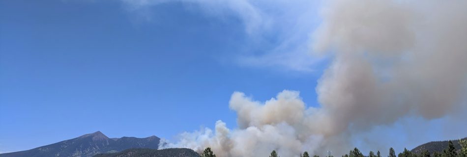 A smoke plume coming up on the east side of a peak.